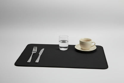 Black placemat with cutlery and a cup on a white kitchen counter.